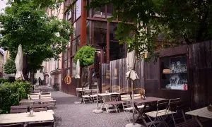 Tavoli all'aperto e ombrelloni di fronte al Batzen Bräu, con un'architettura industriale e un'atmosfera rilassata.