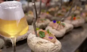 Un bicchiere di birre ale italiane accanto a tartare di pesce su pietre.