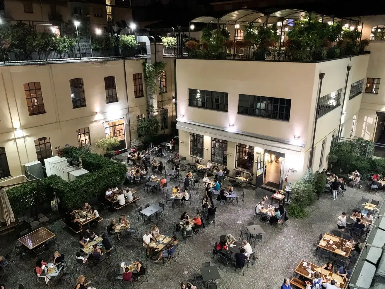 Serata vivace al birrificio La Piazza, con tavoli all'aperto pieni di gente che gode della buona compagnia e delle birre artigianali.