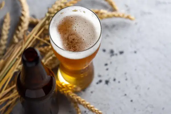 Boccale di birra dorata con schiuma abbondante, accanto a una bottiglia scura e spighe di grano. Un omaggio ai birrificio styles.