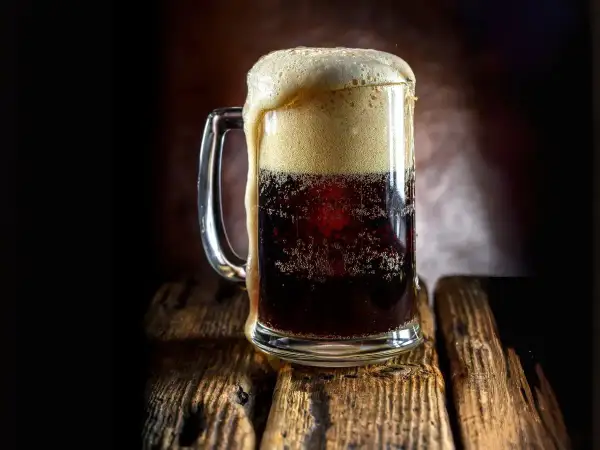 Boccale di birra scura con schiuma abbondante, forse la birra americana più famosa, su un tavolo di legno rustico.