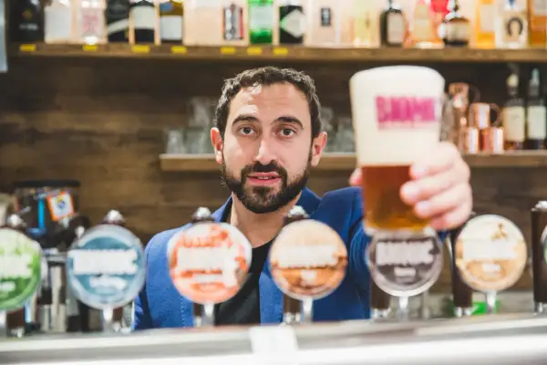 Barista con una birra in mano, pronto a versare nei bicchieri. Dietro di lui, una selezione di birre artigianali.