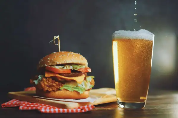 Un succulento hamburger con formaggio fuso e lattuga, accompagnato da una birra bionda spumeggiante.