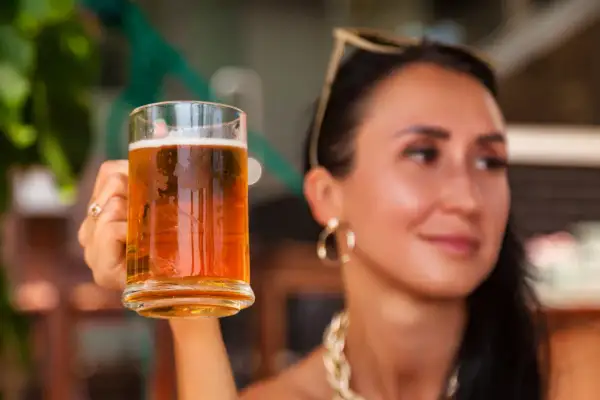 Donna sorridente con in mano un boccale di birra weiss, perfetta per godersi una giornata di sole.