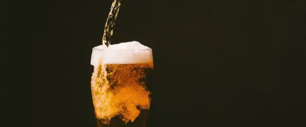 Birra dorata versata in un bicchiere, con schiuma abbondante e bollicine che salgono. Un piacere rinfrescante, ricco di sali minerali.