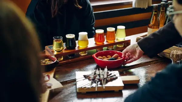 Degustazione di birre pregiate: un assortimento di diverse birre in bicchierini, accompagnate da stuzzichini e spiedini su un tavolo di legno.